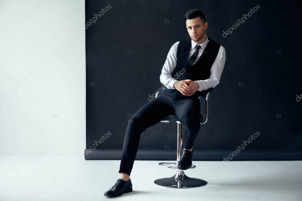 Elegant confident man posing and sitting on chair on black and white background. success concept                   
