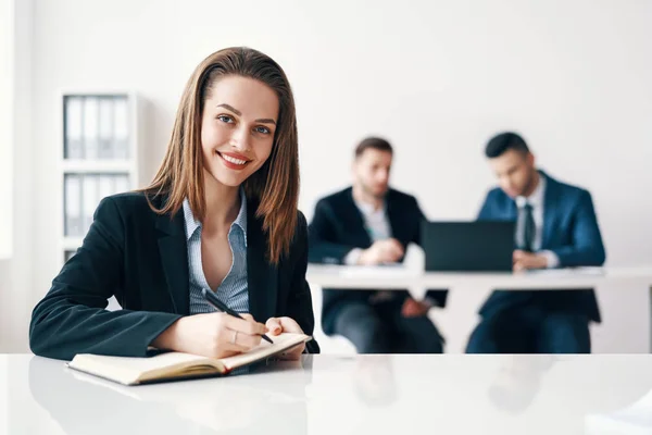 快乐微笑的商务女性画像坐在办公室里 与她的商业团队在背景上做笔记 领导力和成功理念 — 图库照片