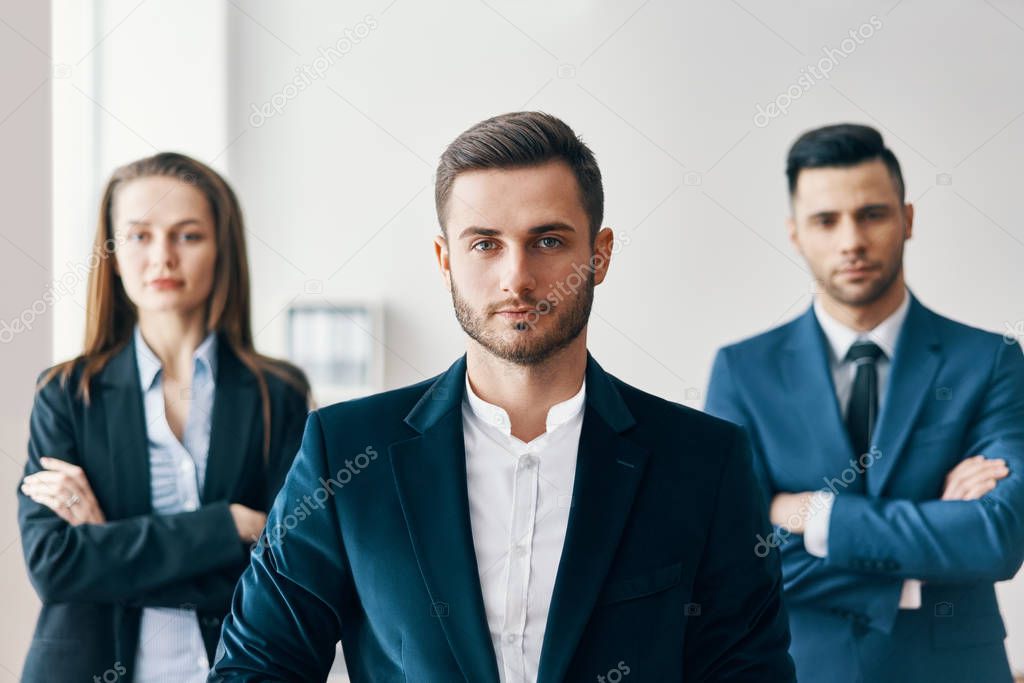 Portrait of confident handsome businessman in office with his team on background. Leadership and success concept