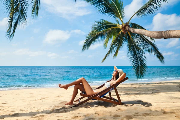 デッキチェアで熱帯のビーチで日光浴をする若い女性 — ストック写真