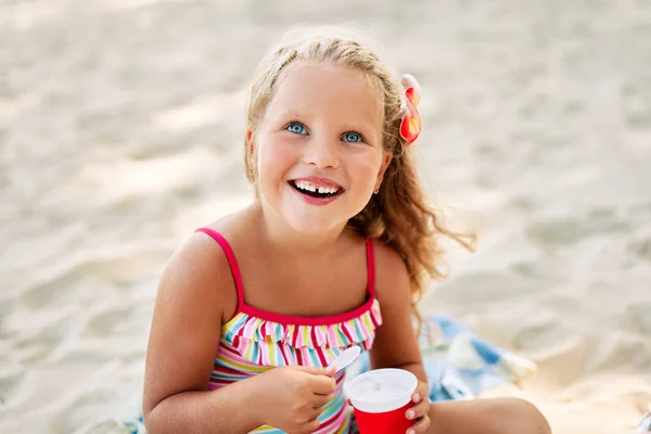 砂浜でアイスクリームを食べるかわいいブロンドの小さな女の子 — ストック写真