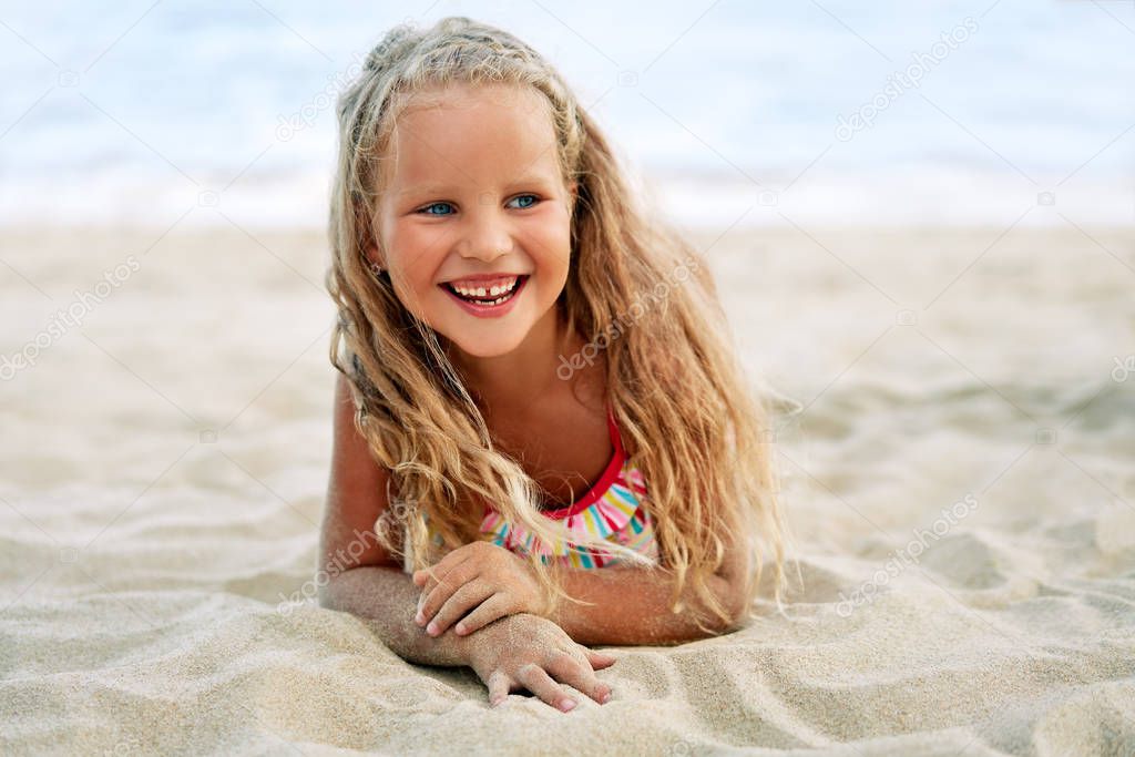 Adorable little blonde girl relaxing on sandy beach enjoying sea. Smiling pretty child posing on beach. 