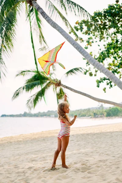 ヤシの木の下で熱帯のビーチで凧を飛ばして幸せな小さな女の子 ビーチの楽しみ 幸せな子供時代の概念 — ストック写真