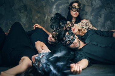 Maskeli karnaval maskeleri içinde arkadaş grubu partiden sonra rahatlatıcı katta yatıyordu. Venedik maskesi takan kadın ve erkekler.