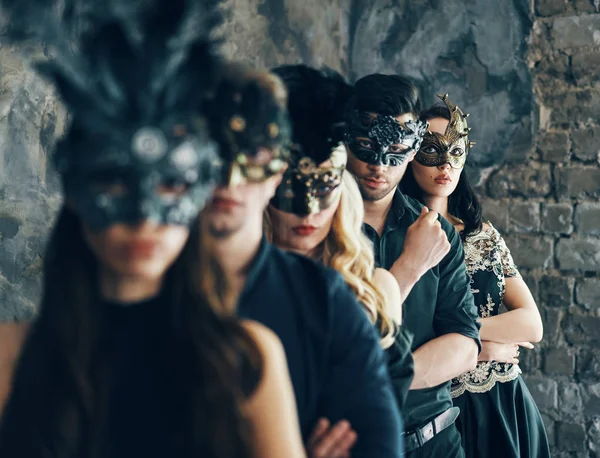 Group of young people in masquerade carnival masks posing in studio, standing in row. Fashion photo concept.