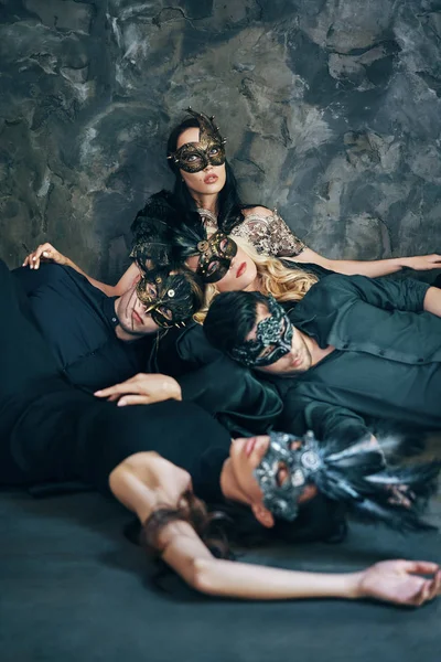 一群朋友在伪装的狂欢节面具躺在地板上放松后党 戴威尼斯面具的男女 — 图库照片
