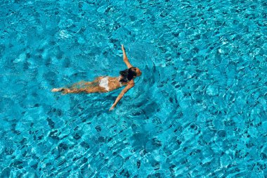 Yüzme havuzunda yüzen beyaz bikinili genç ince kadının üst görünümü