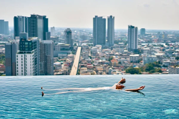 Young woman relaxing in rooftop swimming pool and floating in water