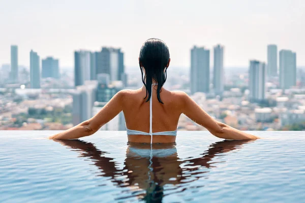 rear view of woman relaxing at edge of rooftop swimming pool