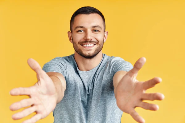 Handsome happy man with open hand ready for hugs on yellow background. Emotions concept