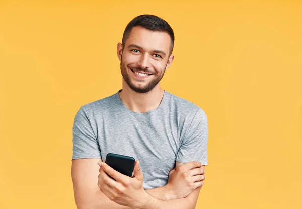 Handsome smiling man holding mobile phone and looking to camera in yellow studio background. Communication concept