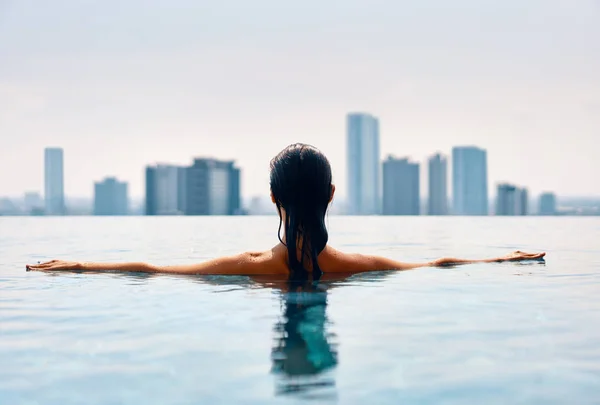 Back view of young woman swimming in swimming pool on rooftop