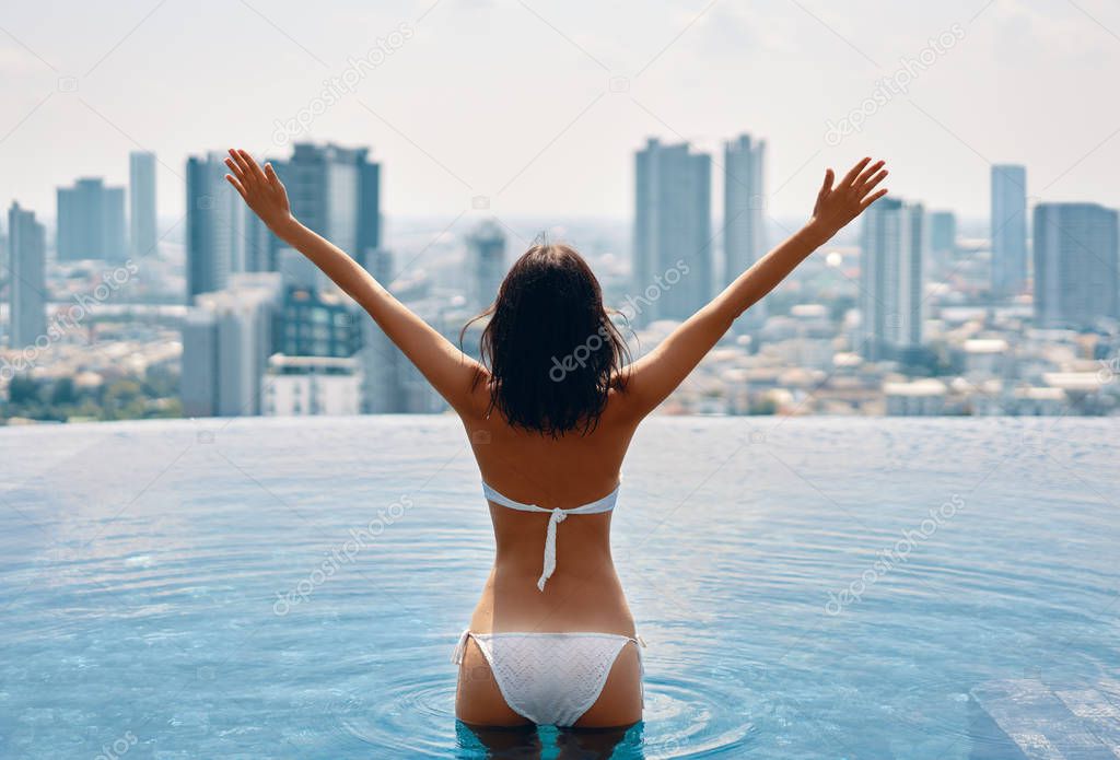 Back view of woman with raised arms in swimming pool on rooftop 