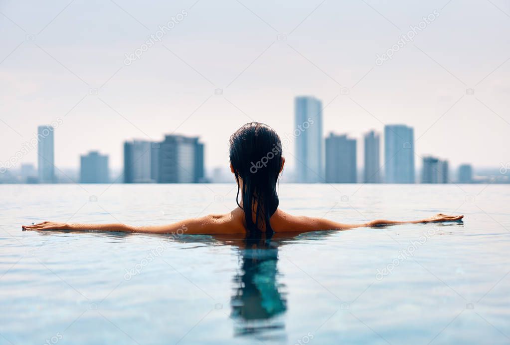 Back view of young woman swimming in swimming pool on rooftop                             
