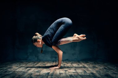 Yoga yapan genç bir kadın karanlık odada asana 'ya poz veriyor. Bakasana. 