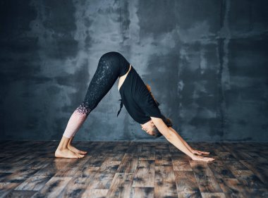 Yoga yapan çekici genç bir kadın koyu arka planda köpek Asana 'nın karşısında dikiliyor.              