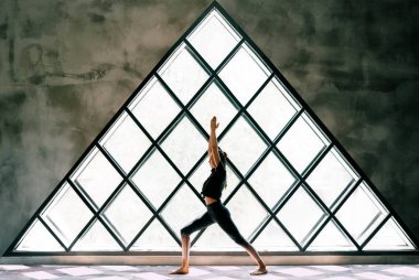 Genç ve güzel bir kadın yoga yapıyor. Asana Savaşçısı. Geniş üçgen pencereye poz veriyor..