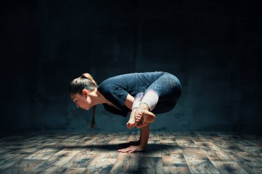 Yoga yapan genç bir kadın karanlık odada vinç pozu veriyor. Parsva Bakasana egzersizi. 