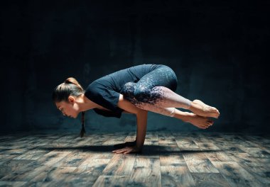 Yoga yapan genç bir kadın karanlık odada vinç pozu veriyor. Parsva Bakasana egzersizi. 