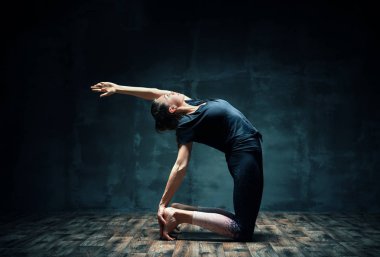 Yoga yapan genç bir kadın karanlık odada yarı deve pozu veriyor. Ardha Ushtrasana egzersizi. 