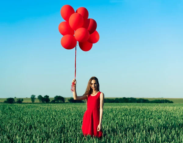 Mladá Žena Červených Šatech Stojící Zeleném Poli Červenými Balónky — Stock fotografie