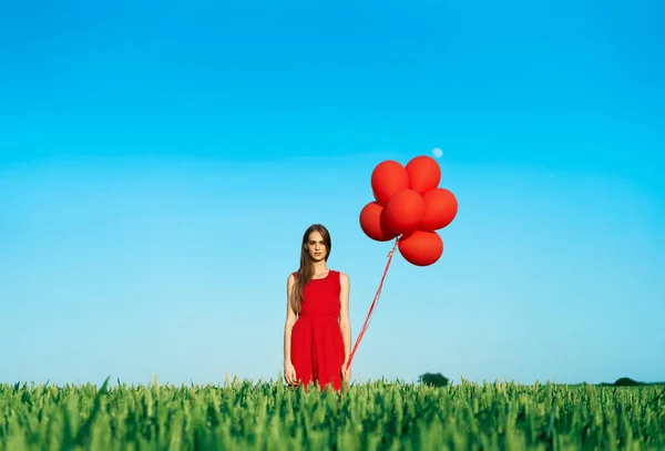 Młoda Kobieta Czerwonej Sukience Stojącej Zielonym Polu Czerwonymi Balonami — Zdjęcie stockowe