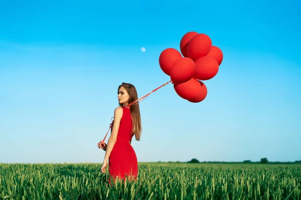 赤い風船で緑の畑に赤いドレスを着た若い女性が — ストック写真