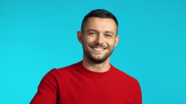 Yakışıklı genç adam gülümsüyor ve mavi arka planda barışı işaret ediyor.