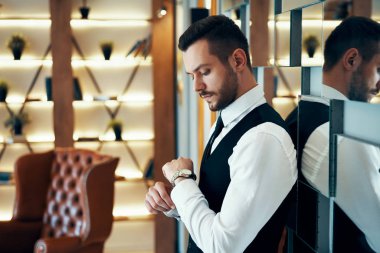 Koyu renk takım elbiseli yakışıklı iş adamı saatine bakıyor.