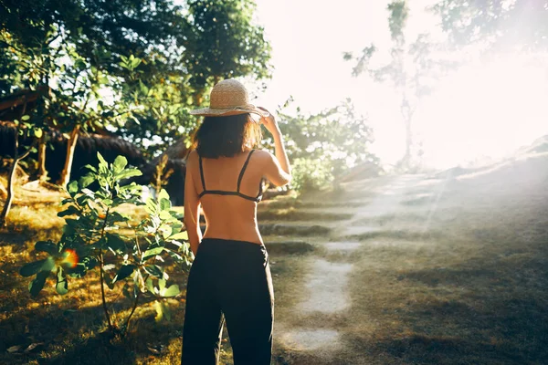 Vista posteriore della giovane donna in cappello di paglia che sale le scale nel verde parco tropicale alla luce del sole — Foto Stock