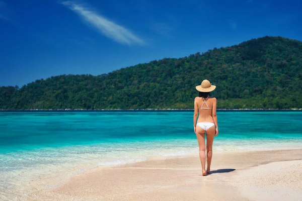 Beautiful young woman in white bikini and straw hat walking on tropical beach in paradise island — Stock Photo, Image