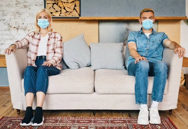 Man och kvinna i facemask sitter på soffan hemma — Stockfoto