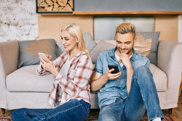 Giovane coppia sorridente che si rilassa sul divano con smartphone a casa — Foto Stock