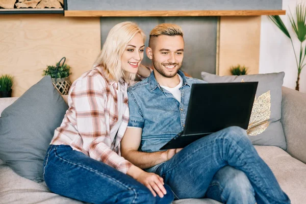 Χαρούμενα νεαρό ζευγάρι με φορητό υπολογιστή surfing στο διαδίκτυο κάθεται στον καναπέ — Φωτογραφία Αρχείου