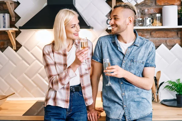 Joven pareja feliz bebiendo champán y disfrutando de la compañía de los demás en la cocina en casa —  Fotos de Stock