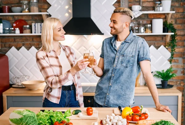 Młoda szczęśliwa para pije szampana i cieszy się towarzystwem w kuchni w domu — Zdjęcie stockowe