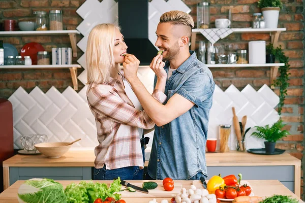 Mooi jong paar is het voeden van elkaar en glimlachen tijdens het koken in keuken thuis — Stockfoto