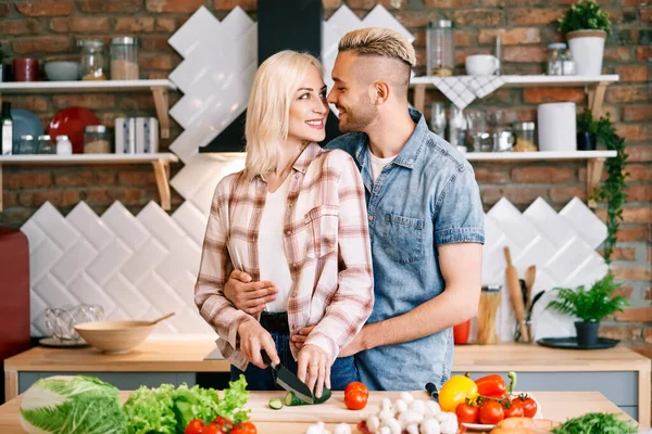 Улыбающаяся молодая пара готовит вместе вегетарианскую еду на кухне дома — стоковое фото