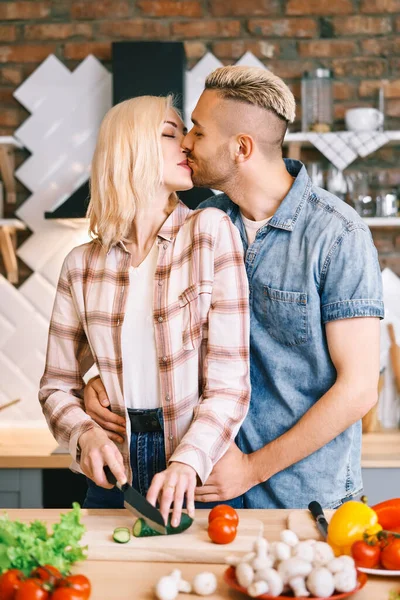 Casal jovem beijando e cozinhando juntos refeição vegetariana na cozinha em casa — Fotografia de Stock