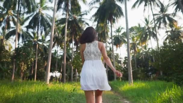 Mujer joven feliz en vestido blanco corriendo en la selva entre palmeras en la isla tropical — Vídeos de Stock