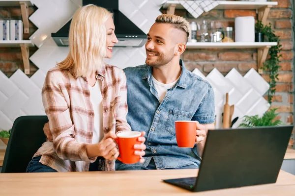 Feliz pareja beber café y el uso de ordenador portátil relajarse juntos en su cocina —  Fotos de Stock