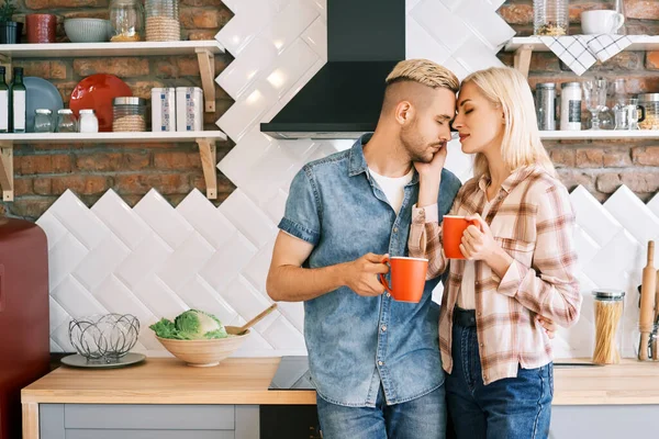 Jong gelukkig paar in liefde drinken koffie in de ochtend omarmen in de keuken thuis — Stockfoto