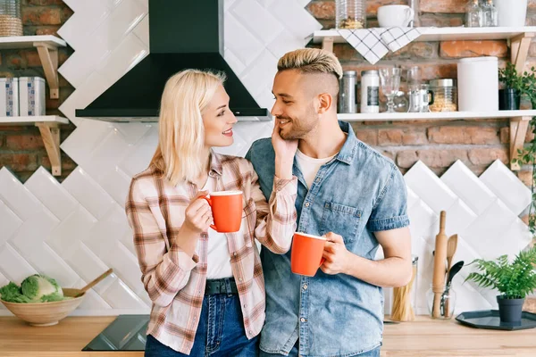 Fiatal boldog pár szerelmes iszik kávét reggel ölelkezve a konyhában otthon — Stock Fotó