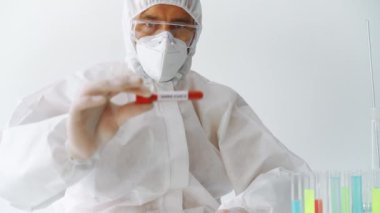 Koruyucu kıyafetli doktor Sars-CoV-2 'nin kan örneği tüpünü enfekte ettiğini gösteriyor.