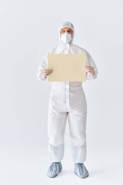 Koruyucu tıbbi giysili doktor, metin için kopyalama alanı olan boş bir levha gösteriyor.