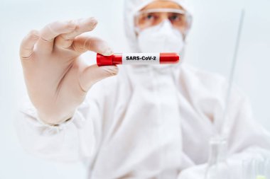 Doctor in protective suit showing coronavirus infected blood sample test tube clipart