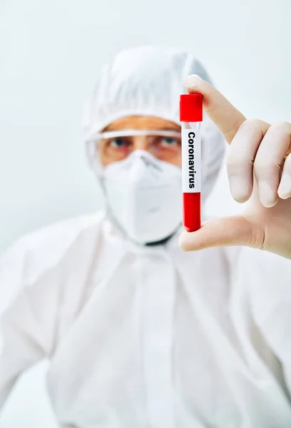 Врач в защитном костюме показывает коронавирус, инфицированный пробиркой крови — стоковое фото