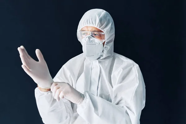 Doctor en traje médico protector se pone guantes estériles quirúrgicos protectores en su brazo —  Fotos de Stock