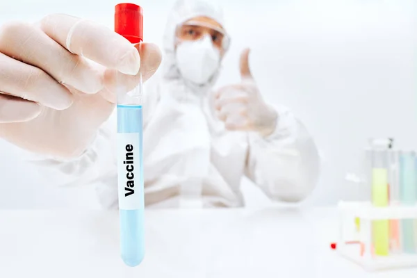 Vědec v PPE držení vakcíny proti infekčním onemocněním a ukazující palec nahoru — Stock fotografie