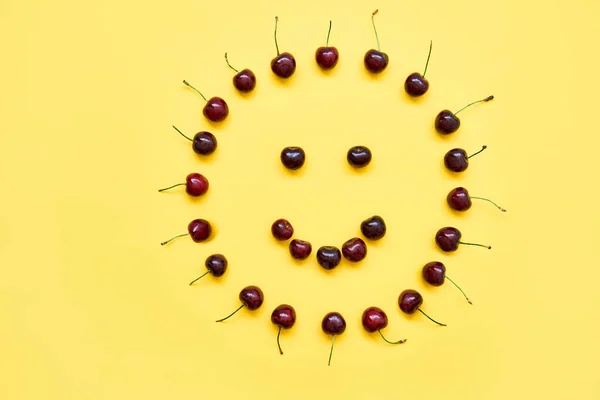 Cerezas dulces en forma de cara sonriente al sol sobre fondo amarillo — Foto de Stock